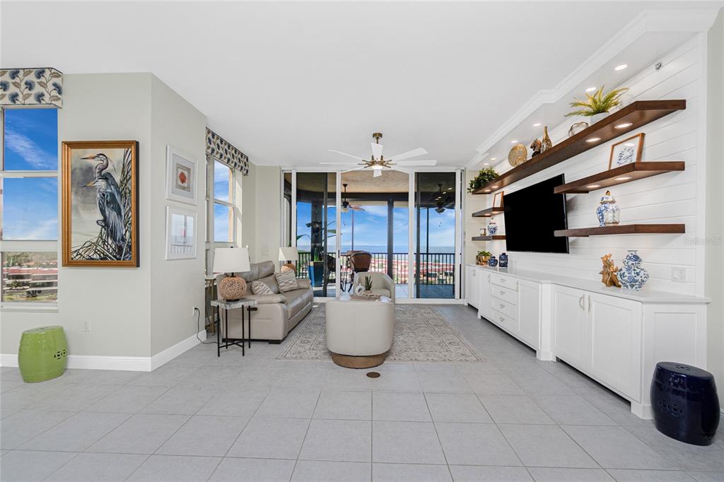 A living room features a white shiplap wall with floating shelves, a television, and balcony views — 3313 SUNSET KEY CIR UNIT 701, PUNTA GORDA, FL
