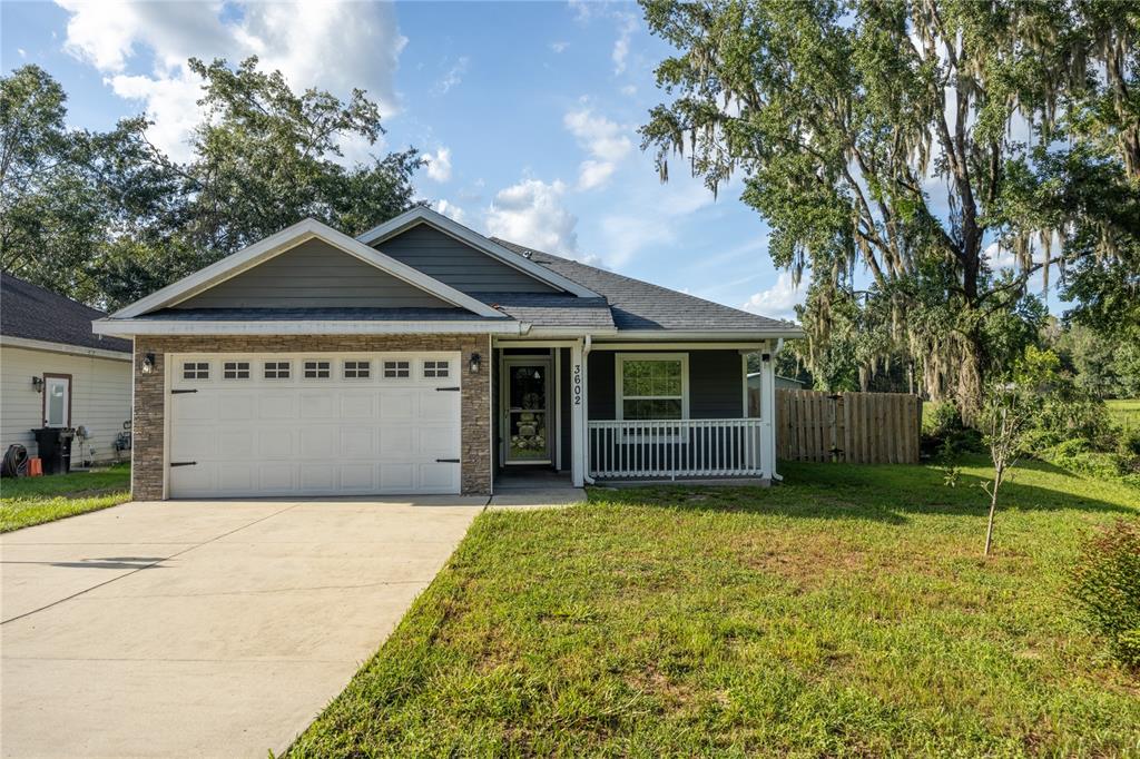 A single-story house with a garage, stone accents, and a front porch under a tree — 3602 NW 55TH LANE, GAINESVILLE, FL