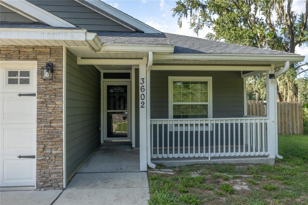 The exterior of a house features gray siding, stone accents, a covered porch, and a walkway — 3602 NW 55TH LANE, GAINESVILLE, FL