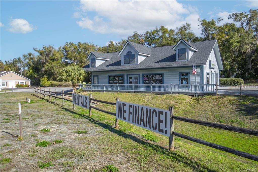 A gray commercial building with dormer windows sits behind a wooden fence with signage — 525 S US HIGHWAY 41, INVERNESS, FL