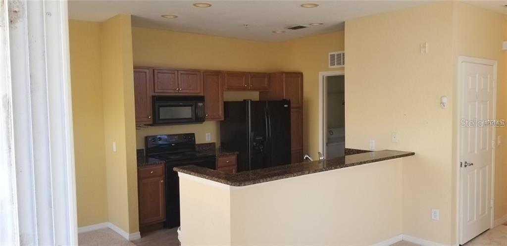 A kitchen features wood cabinets, black appliances, and a granite-topped peninsula breakfast bar — 2532 GRAND CENTRAL PARKWAY UNIT 10, ORLANDO, FL