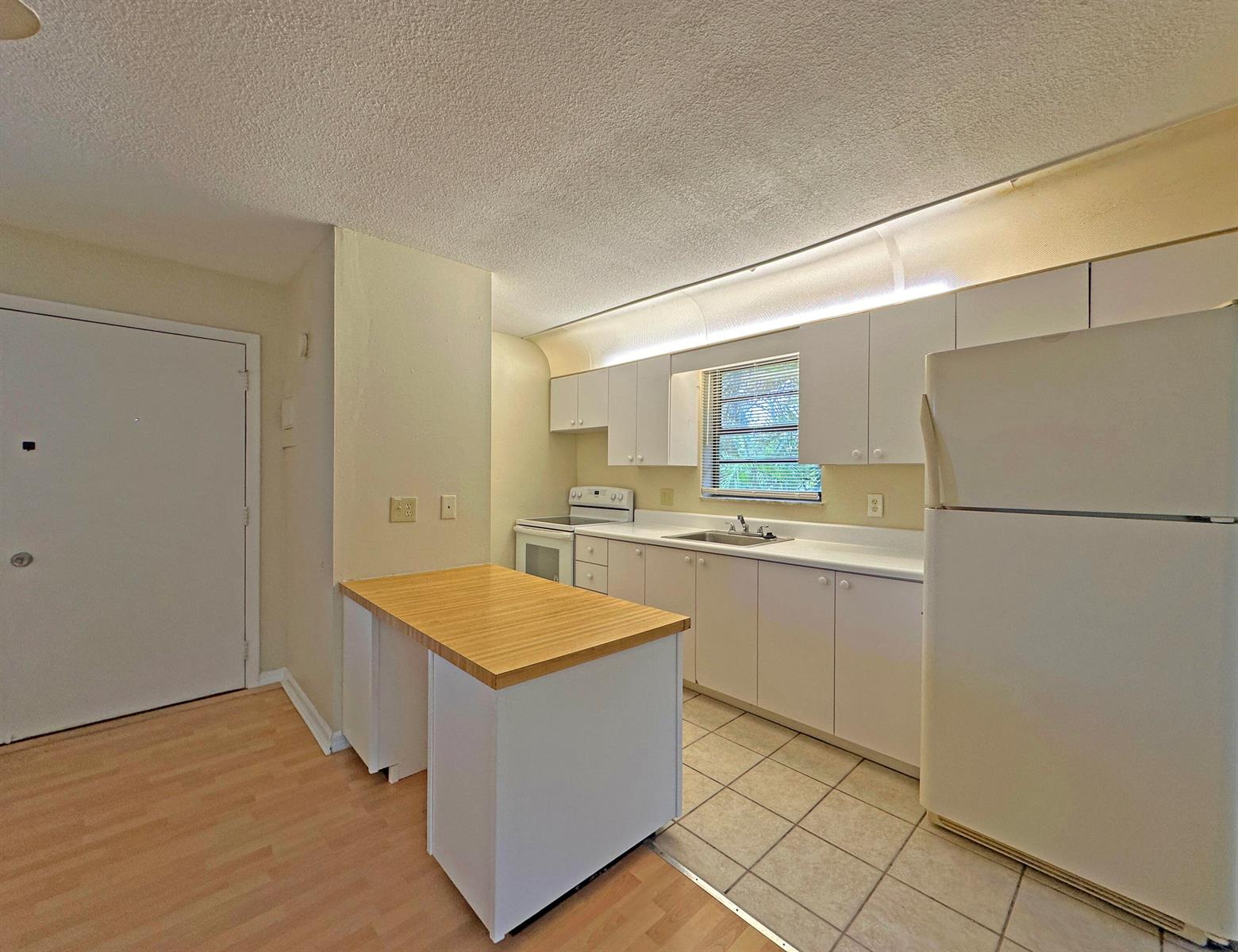 A kitchen features white cabinets, a wood-topped island, tile flooring, and a white refrigerator — 1021 SE Monterey Road # A22, Stuart FL 34994, STUART, FL