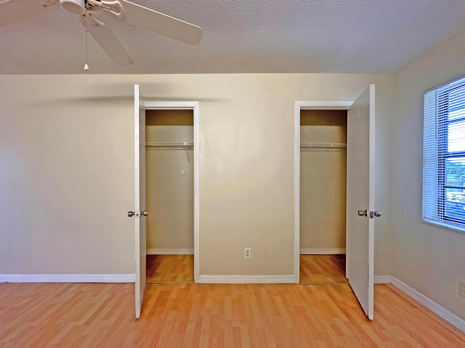A bedroom features light-colored walls, wood-look flooring, a ceiling fan, and two open closets — 1021 SE Monterey Road # A22, Stuart FL 34994, STUART, FL