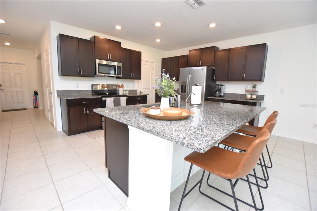 A kitchen features dark wood cabinets, granite countertops, a central island, and three bar stools — 2767 RED EGRET DRIVE, BARTOW, FL