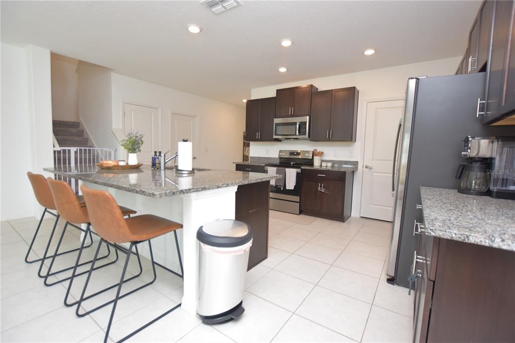 A kitchen features dark wood cabinets, granite countertops, a center island with stools, and tile flooring — 2767 RED EGRET DRIVE, BARTOW, FL