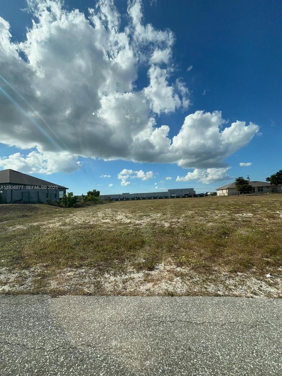 A vacant, grassy residential lot sits under a bright blue sky with large clouds — 2002 NW 3 TER, Cape Coral FL 33993, CAPE CORAL, FL