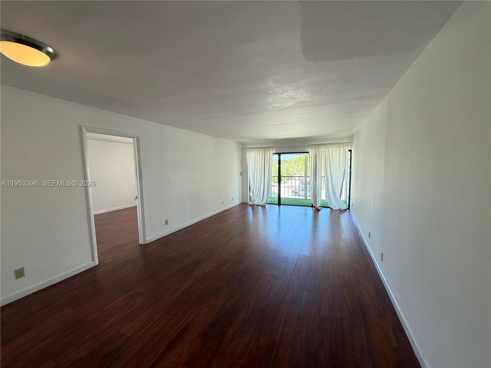 An empty living room features dark wood-look flooring, white walls, and a sliding glass door — 240 Lakeview Dr # 308, Weston FL 33326, WESTON, FL