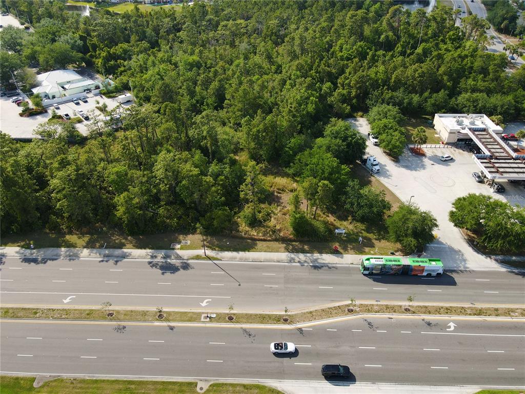 An aerial view shows a wooded vacant lot situated between a gas station and commercial buildings — 11914 INTERNATIONAL DRIVE, ORLANDO, FL