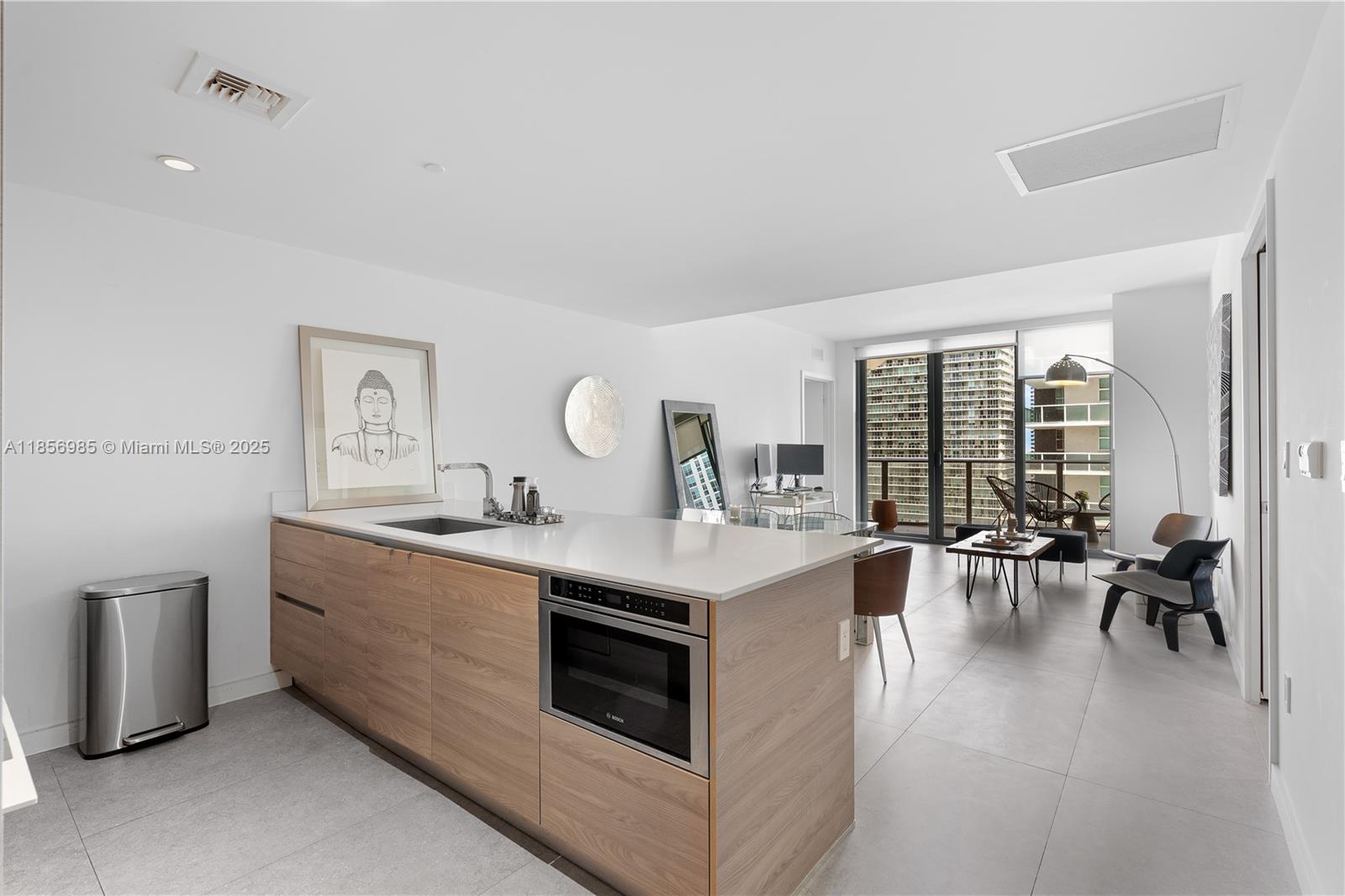 A modern kitchen island with wood cabinetry and a white countertop sits in an open-plan apartment — 1300 S Miami Ave # 2411, Miami FL 33130, MIAMI, FL