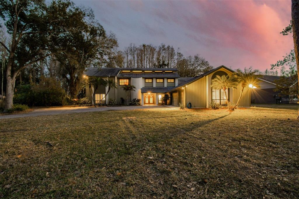 A two-story house with vertical siding and a large front lawn at dusk — 3812 LITTLE ROAD, LUTZ, FL