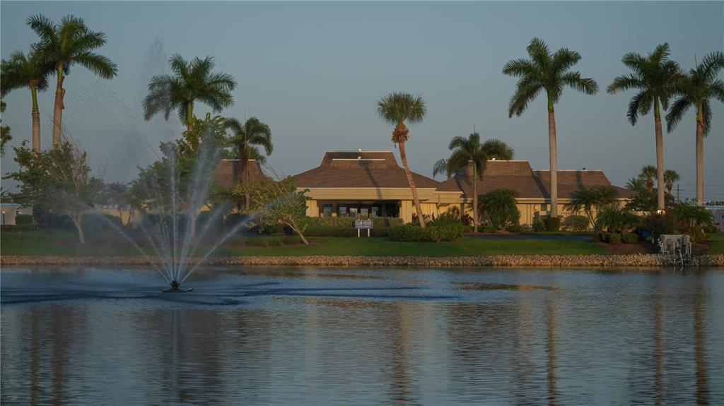 A fountain sprays water in a lake in front of a clubhouse with palm trees — 602 LA JOLLA CIRCLE, NORTH PORT, FL