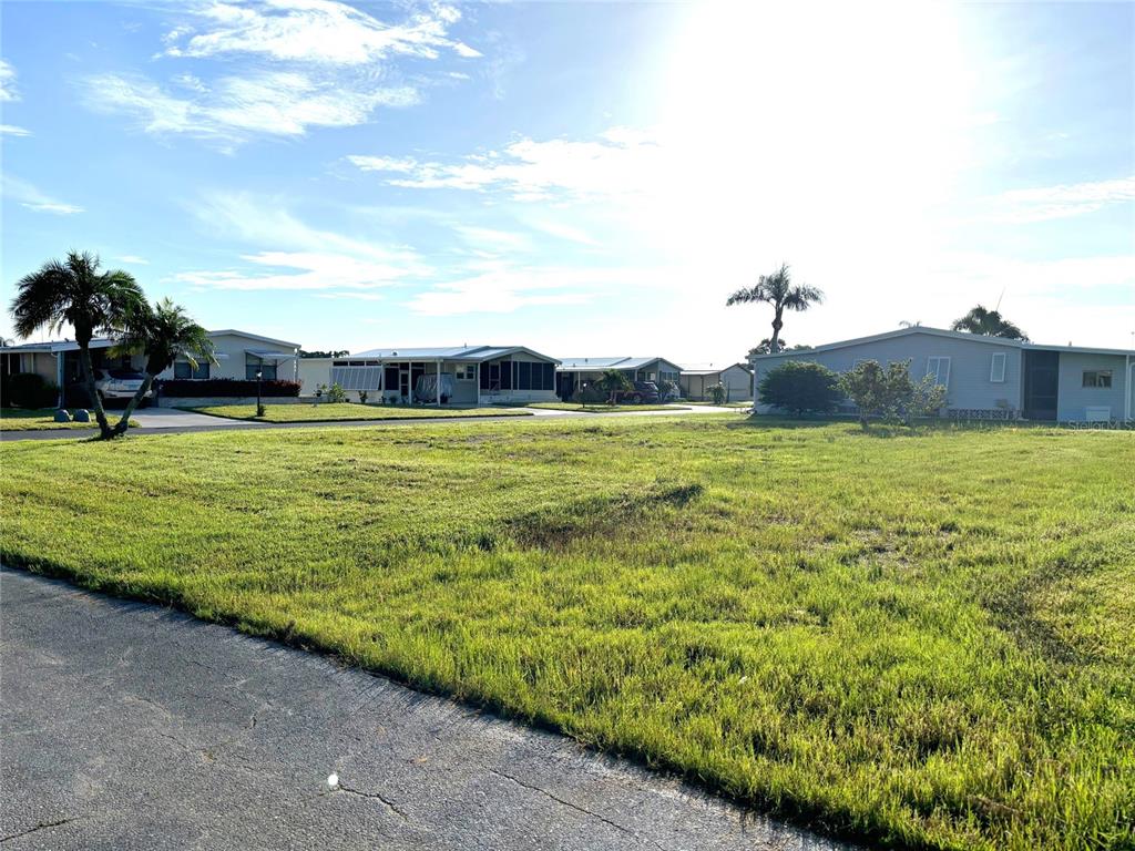 A vacant grassy lot sits in a residential neighborhood with several manufactured homes nearby — 602 LA JOLLA CIRCLE, NORTH PORT, FL