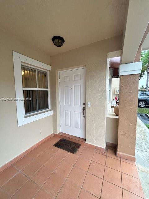 A covered porch features a white front door, a window with blinds, and tiled flooring — 13884 SW 64th St, Miami FL 33183, MIAMI, FL