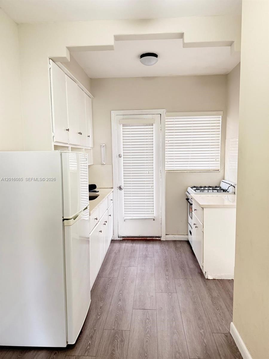 This galley kitchen features white cabinets, a white refrigerator, a gas stove, and wood-look flooring — 1007 Meridian Ave # 9, Miami Beach FL 33139, MIAMI BEACH, FL