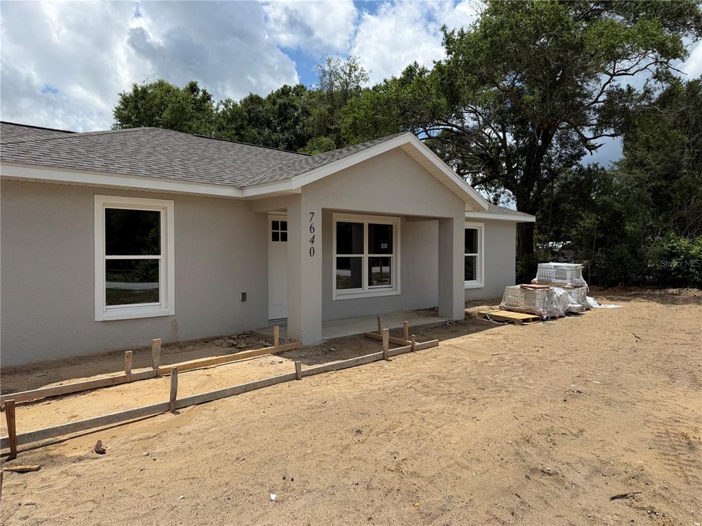 A newly constructed single-story house with a gray stucco exterior and a covered front porch — 7640 SW 14TH STREET, OCALA, FL