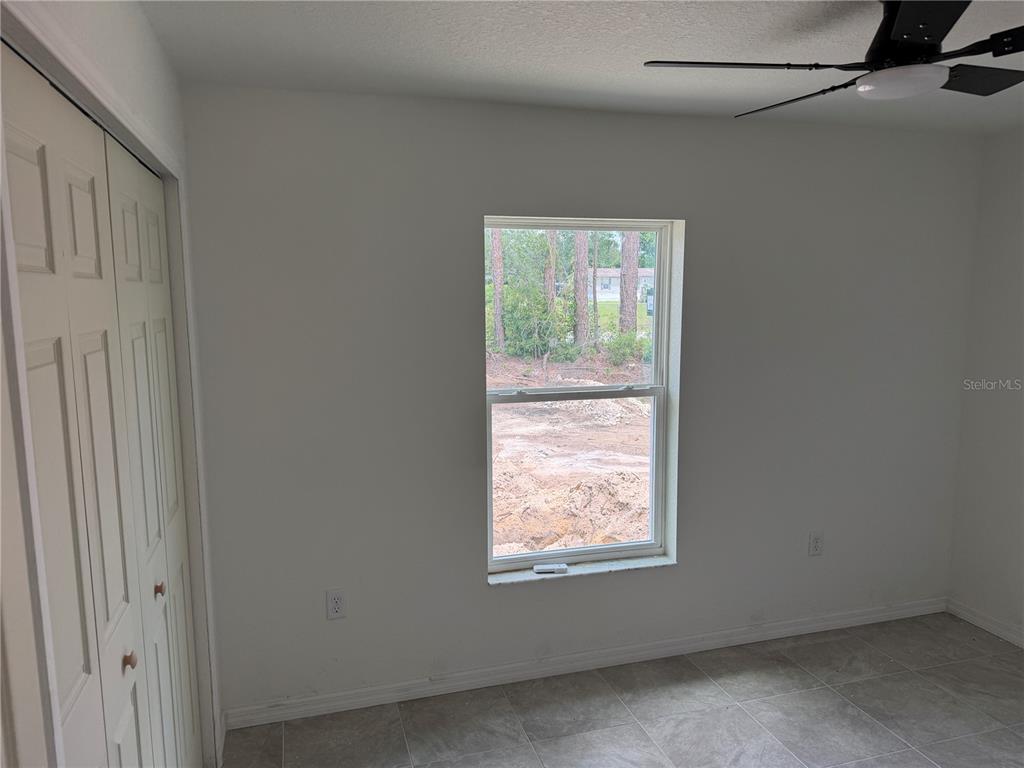 A bedroom with white walls, tile flooring, a ceiling fan, and a window overlooking dirt — 7640 SW 14TH STREET, OCALA, FL