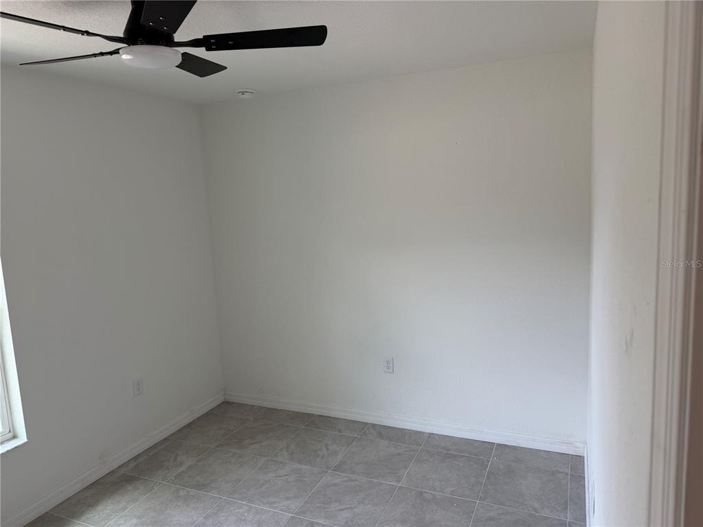 A small, empty room with white walls, gray tile flooring, and a ceiling fan — 7640 SW 14TH STREET, OCALA, FL