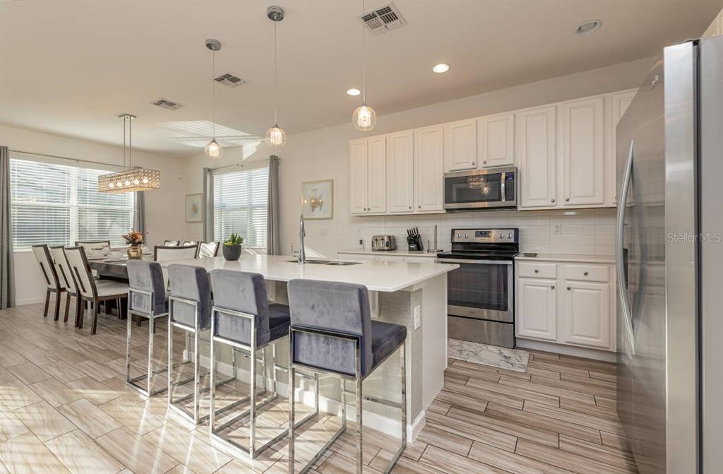 A modern kitchen features white cabinets, stainless steel appliances, and a large island with seating — 2678 CALISTOGA AVENUE, KISSIMMEE, FL