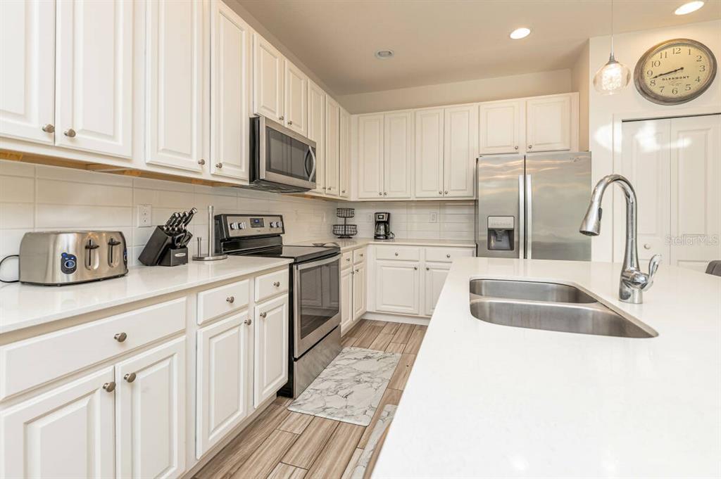 A kitchen with white cabinets, stainless steel appliances, a quartz island, and wood-look tile flooring — 2678 CALISTOGA AVENUE, KISSIMMEE, FL