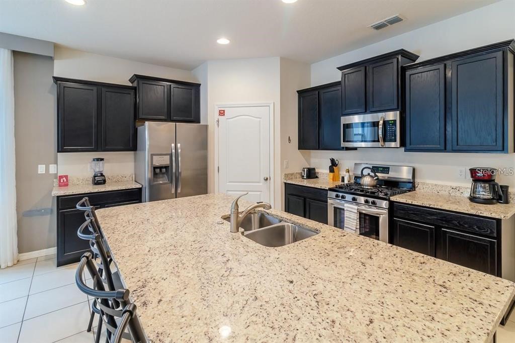 A kitchen features dark cabinets, granite countertops, a large island, and stainless steel appliances — 6047 BROAD OAK DRIVE, DAVENPORT, FL
