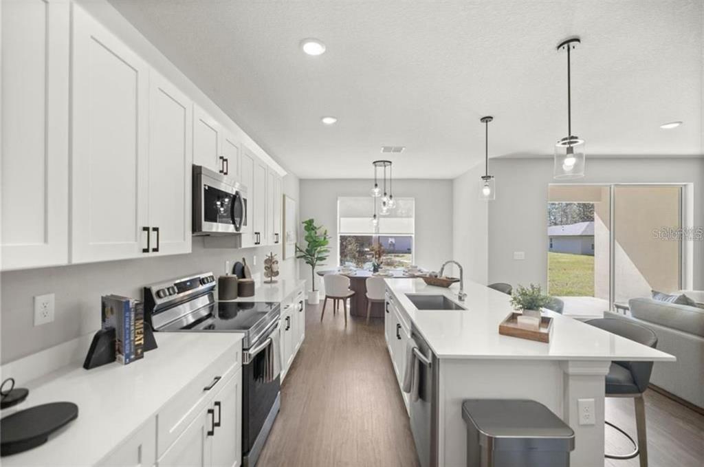 A modern kitchen features white cabinetry, a large center island, and stainless steel appliances — 8703 SW 135TH PL, OCALA, FL