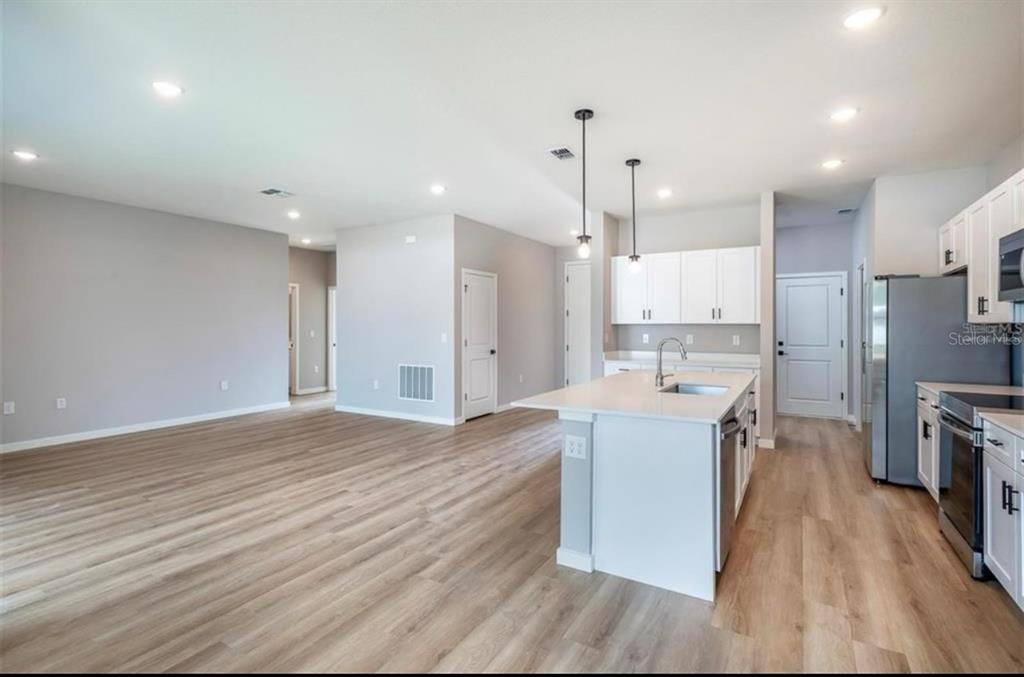 A modern kitchen with a white island and cabinets opens into a spacious living area — 8703 SW 135TH PL, OCALA, FL