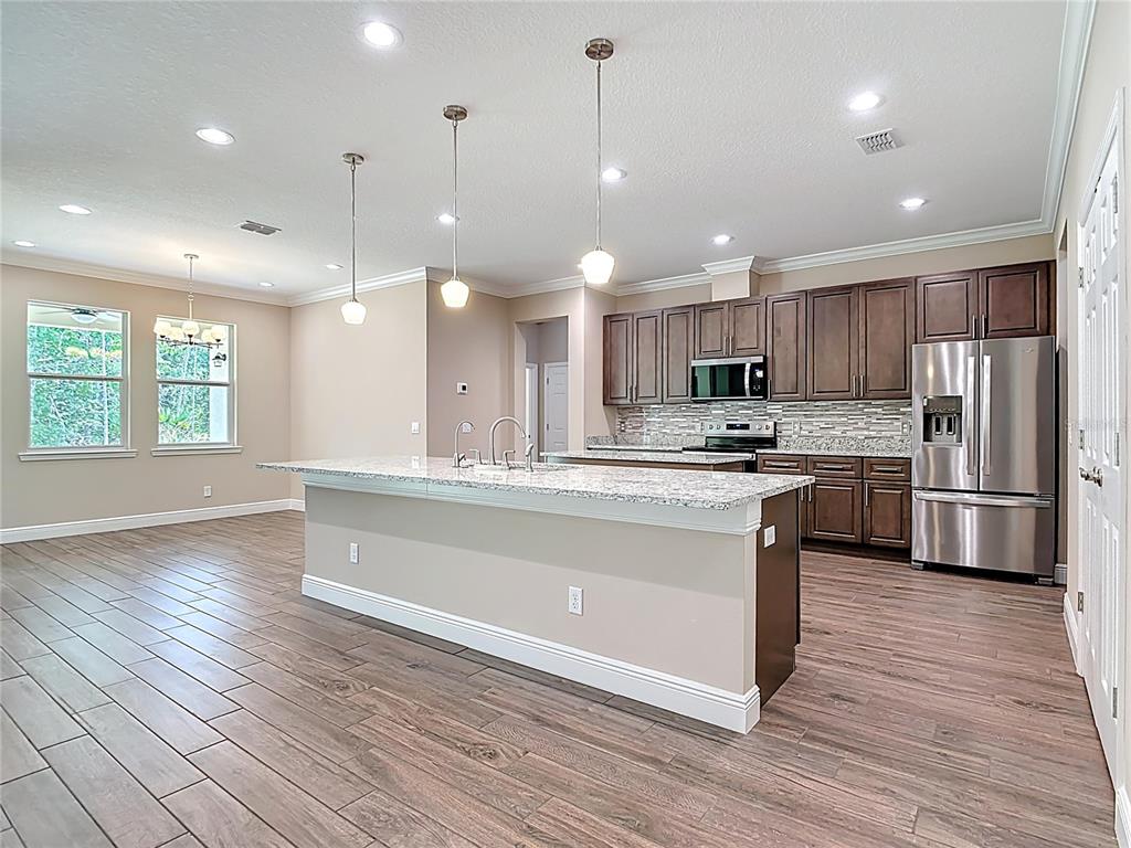A kitchen features dark wood cabinets, granite countertops, a large island, and wood-look tile flooring — 19041 MARDI GRAS STREET, ORLANDO, FL