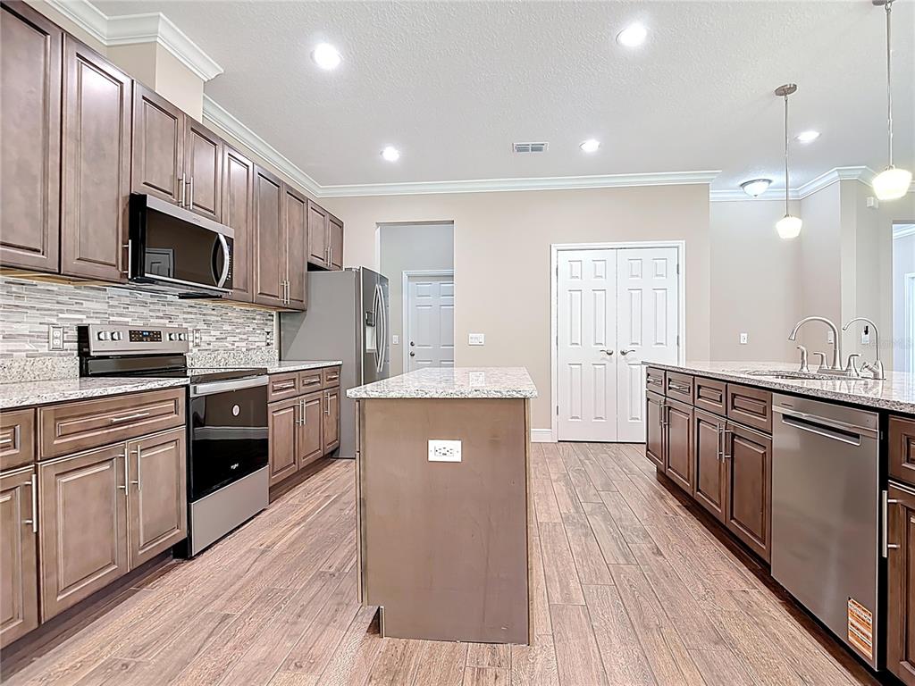 A kitchen features brown cabinets, granite countertops, stainless steel appliances, and wood-look tile flooring — 19041 MARDI GRAS STREET, ORLANDO, FL