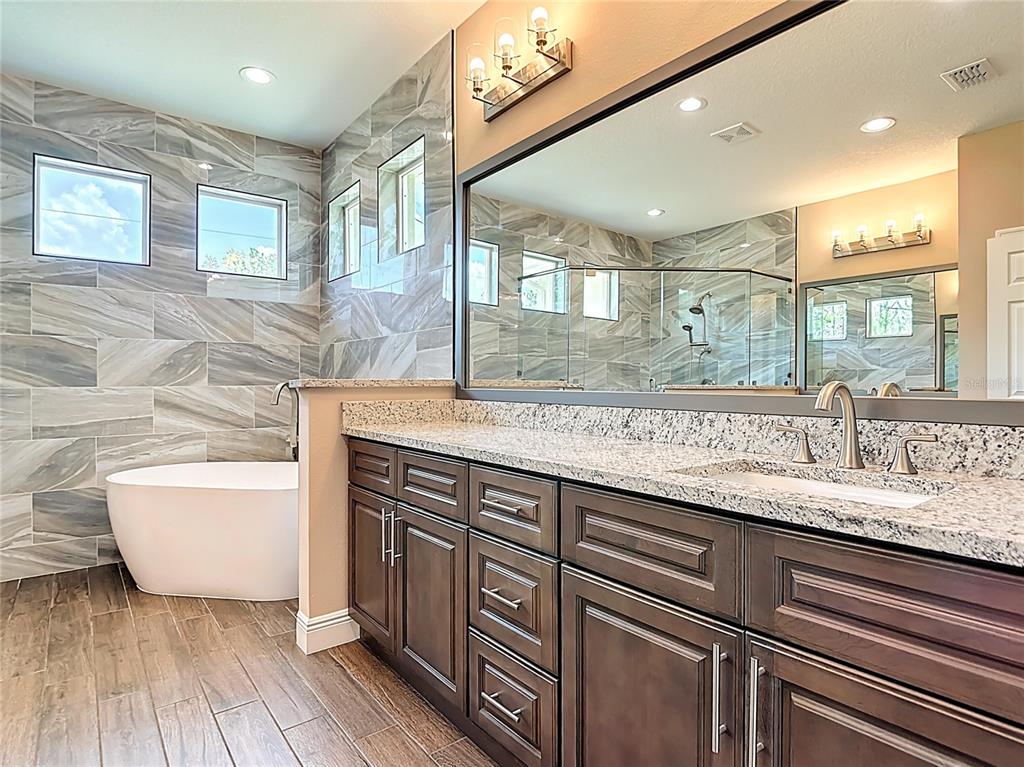 A bathroom features a freestanding tub, a double vanity with granite countertops, and tiled walls — 19041 MARDI GRAS STREET, ORLANDO, FL