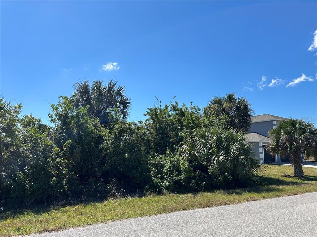 A vacant, overgrown residential lot sits next to a modern house under a blue sky — 13409 GALVESTON AVENUE, PORT CHARLOTTE, FL