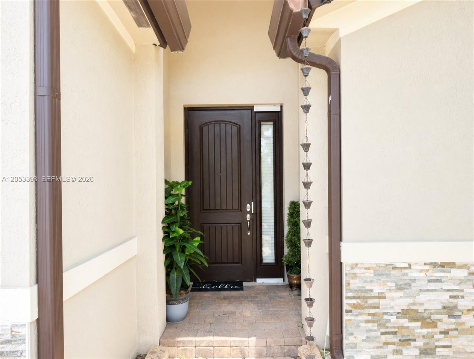 An exterior view shows a front door with a sidelight, a potted plant, and a rain chain — 28151 SW 128th Path, Homestead FL 33033, HOMESTEAD, FL