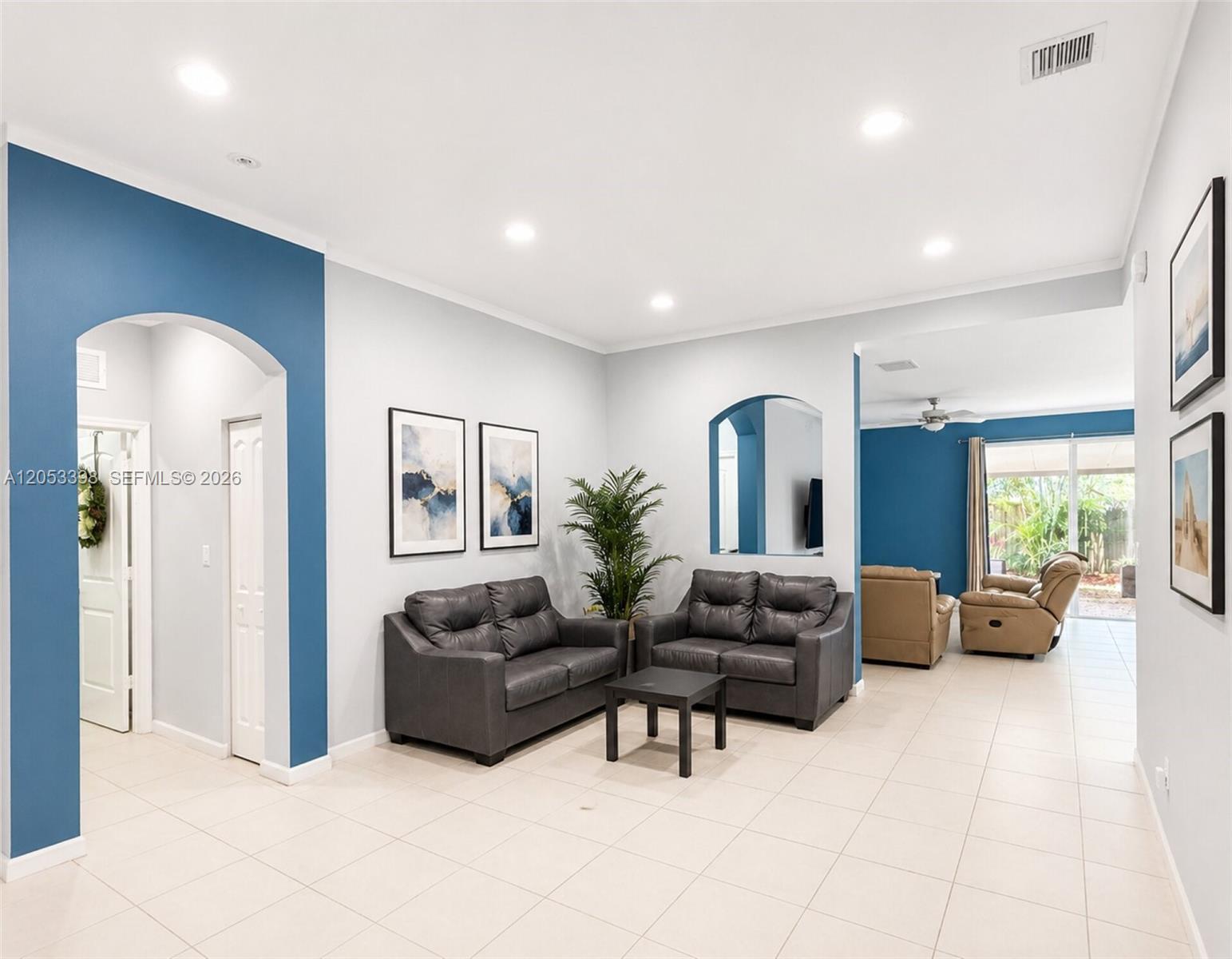 A living room features light-colored tile floors, blue accent walls, and two dark leather sofas — 28151 SW 128th Path, Homestead FL 33033, HOMESTEAD, FL