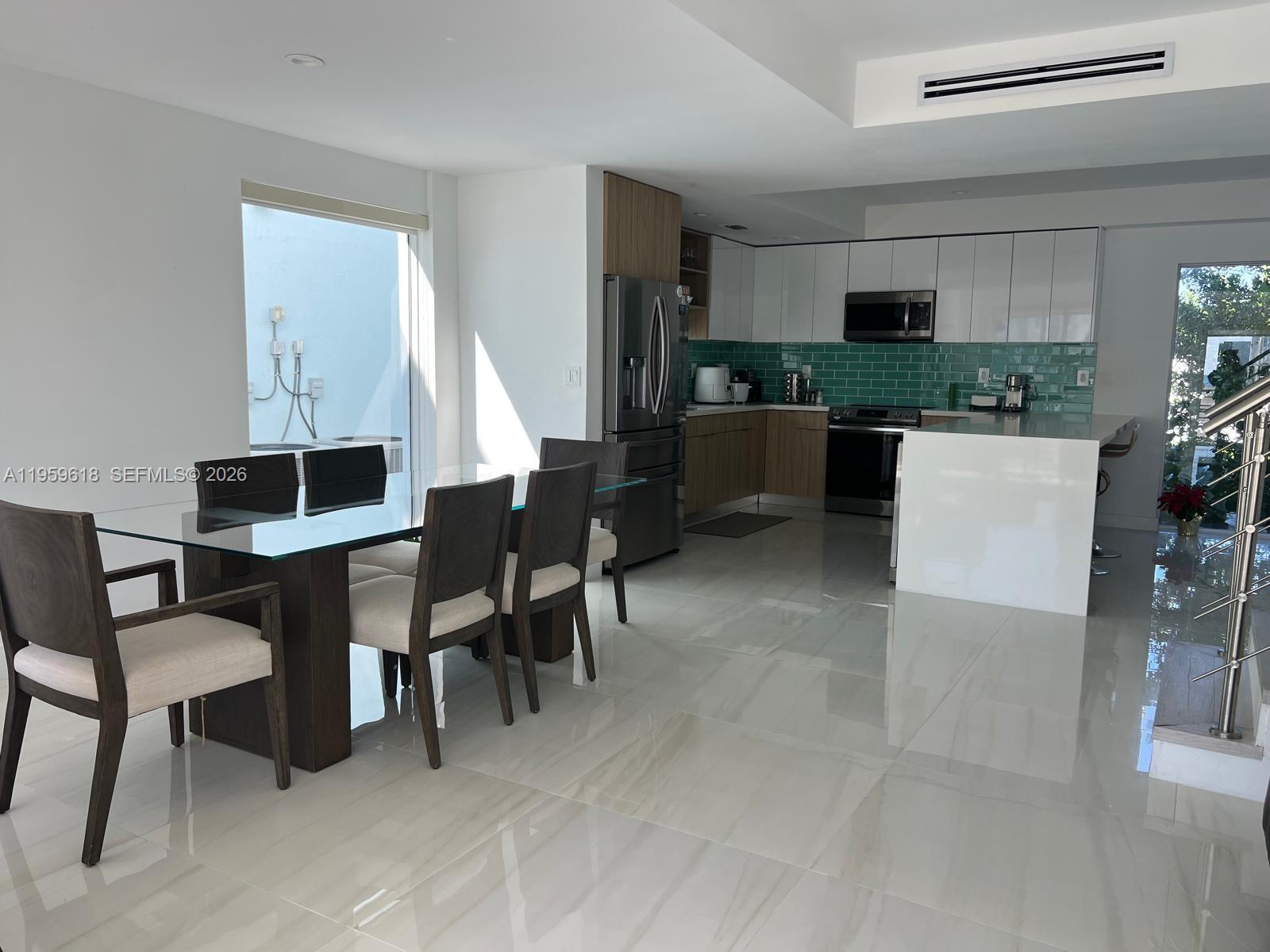 A modern kitchen and dining area feature white cabinetry, a green tile backsplash, and tile flooring — 94825 Overseas Highway, Key Largo FL 33037, KEY LARGO, FL