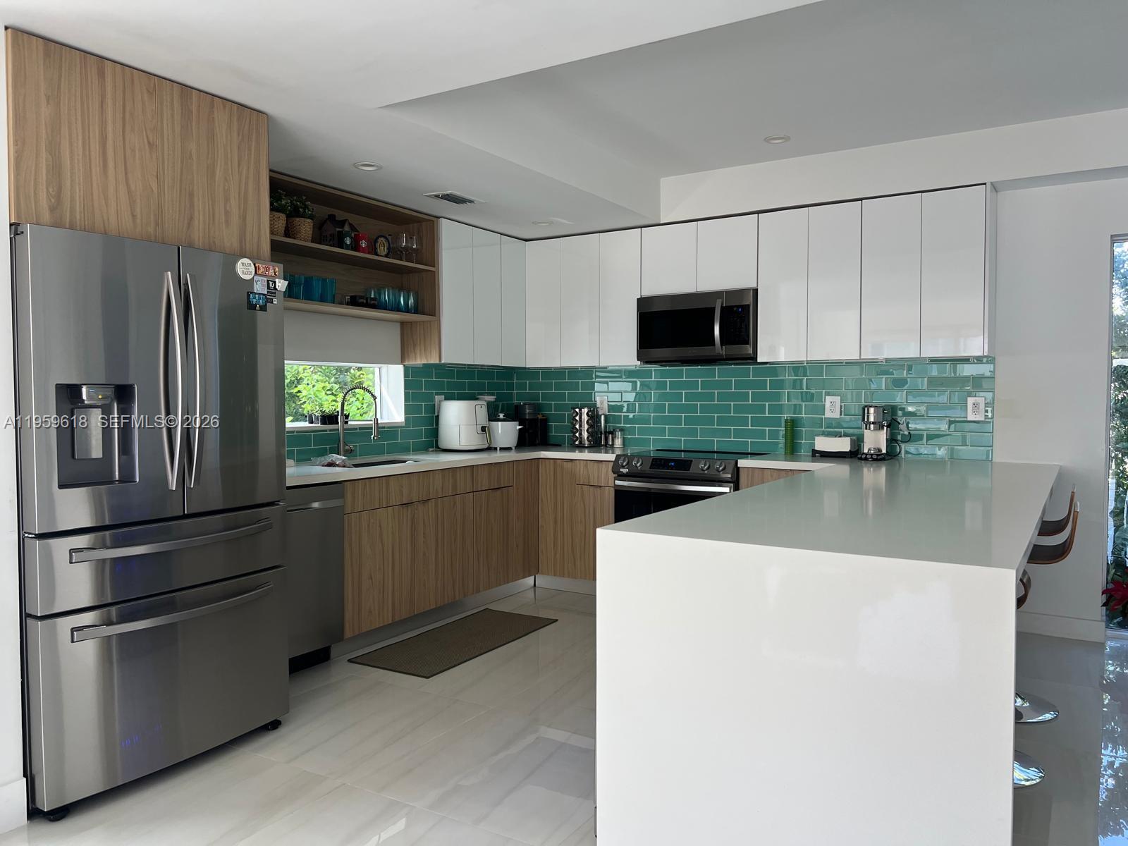 A modern kitchen features white upper cabinets, wood-grain lower cabinets, and a teal subway tile backsplash — 94825 Overseas Highway, Key Largo FL 33037, KEY LARGO, FL