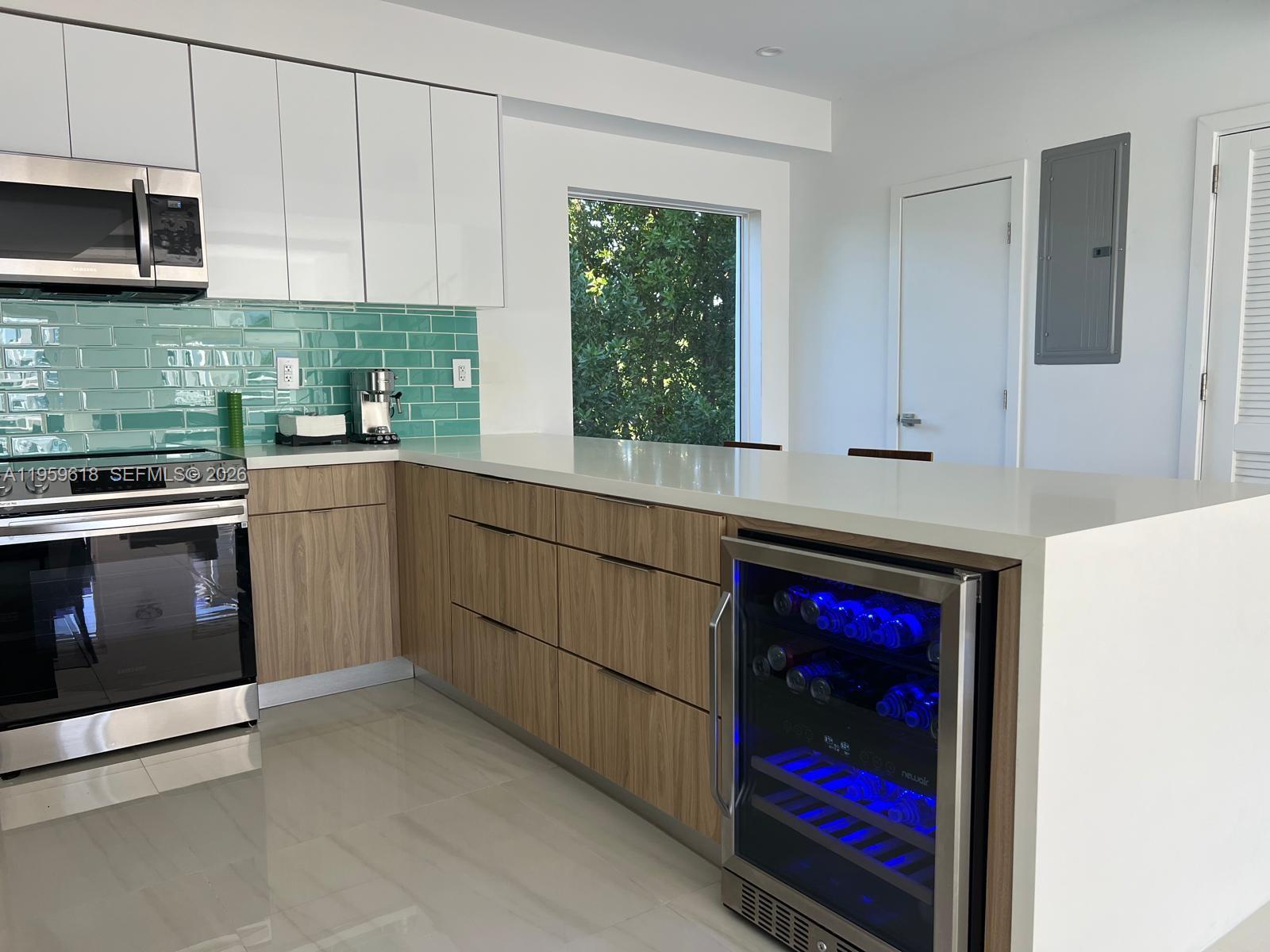A modern kitchen features white upper cabinets, wood-grain lower cabinets, a teal backsplash, and a wine cooler — 94825 Overseas Highway, Key Largo FL 33037, KEY LARGO, FL