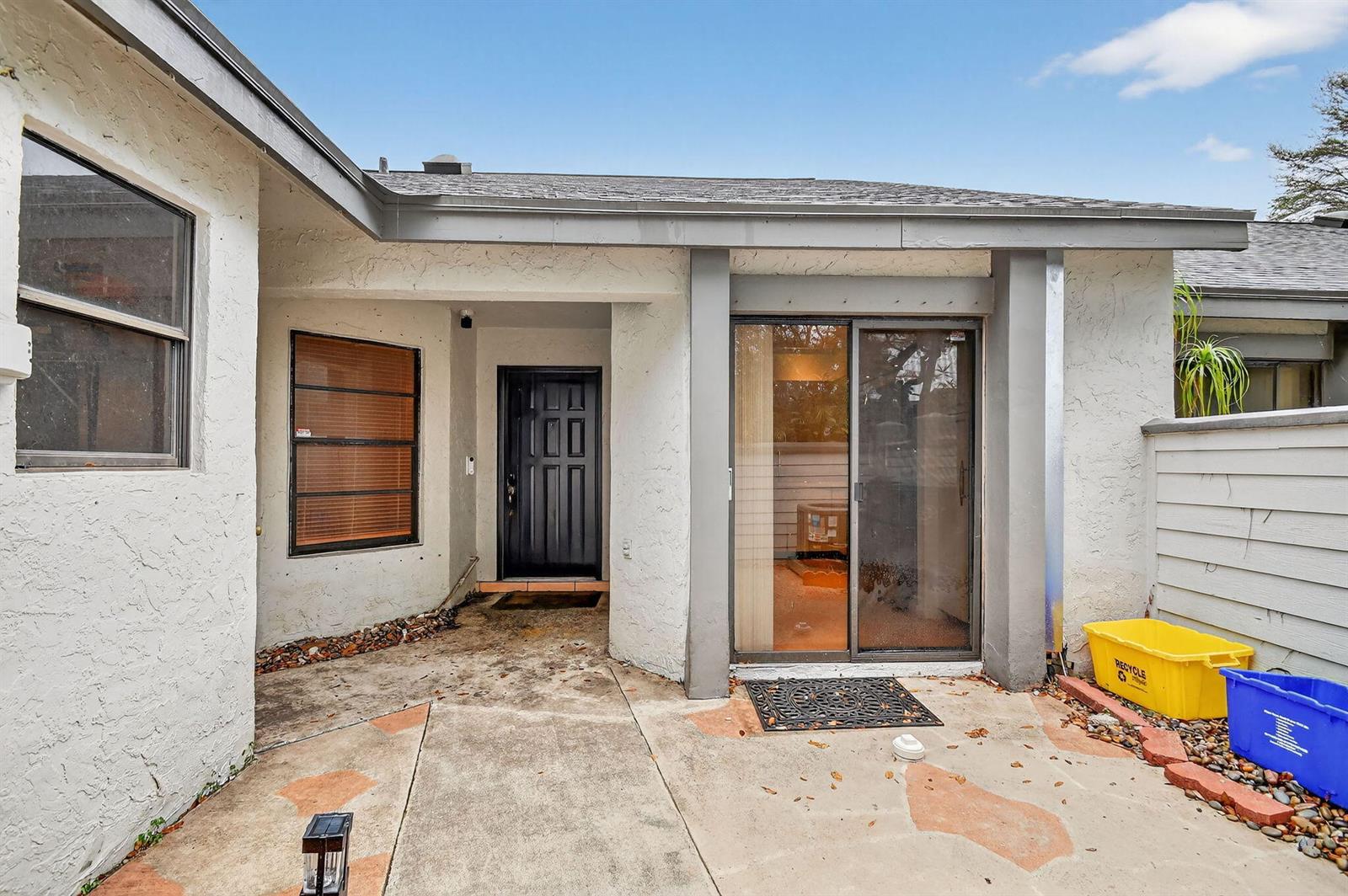 The exterior of a home features a black front door, sliding glass doors, and concrete patio — 2303 Landings Boulevard, FL 33413, FL