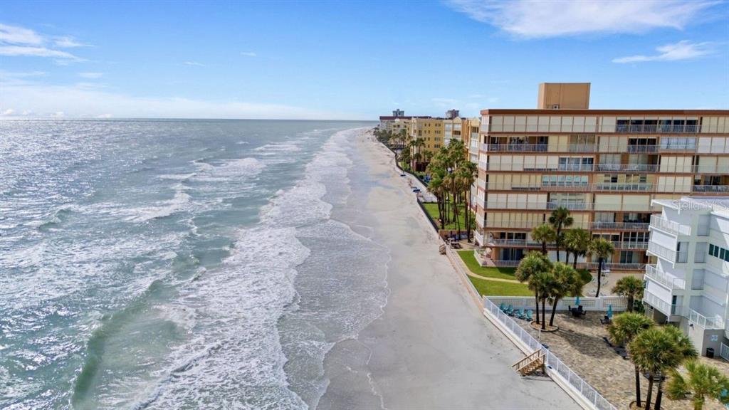 An aerial view of a sandy beach alongside a multi-story residential building and palm trees — 16333 GULF BOULEVARD UNIT 215, REDINGTON BEACH, FL