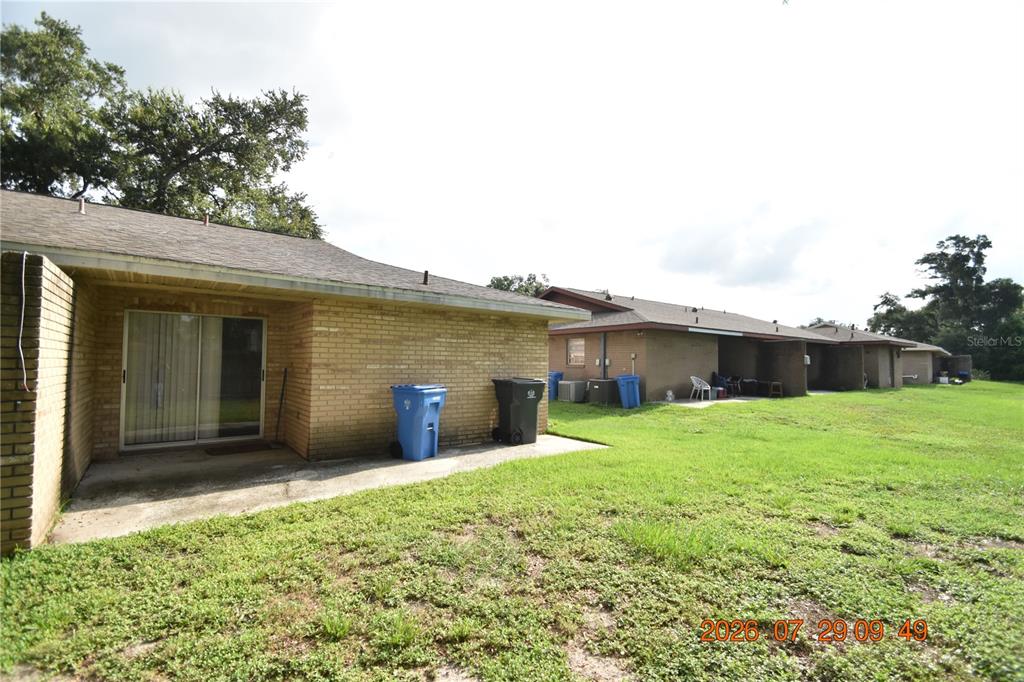 The exterior of a single-story brick building features a concrete patio and two trash bins — 411 BIG CEDAR WAY UNIT A, BRANDON, FL