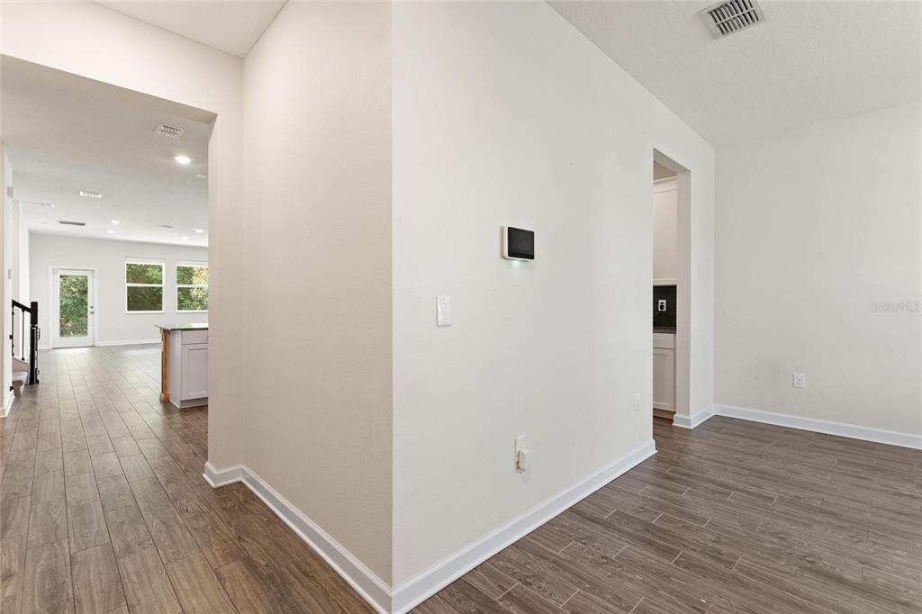 A view of a hallway with wood-look flooring, white walls, and a wall-mounted smart thermostat — 1455 OLYMPIC CLUB BOULEVARD, CHAMPIONS GATE, FL