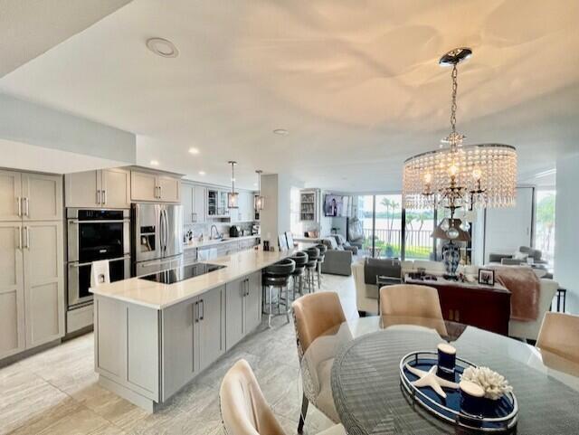 A modern open-concept kitchen and dining area features light cabinetry, a large island, and chandeliers — 2860 S Ocean Boulevard # 301, Palm Beach FL 33480, PALM BEACH, FL