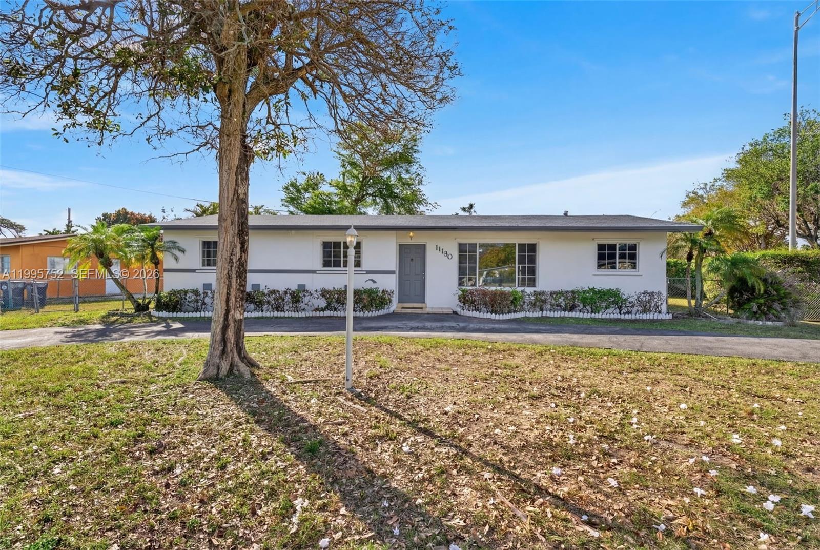 A single-story white house with a gray door and a paved driveway sits on a lawn — 11190 SW 57th St, Miami FL 33173, MIAMI, FL