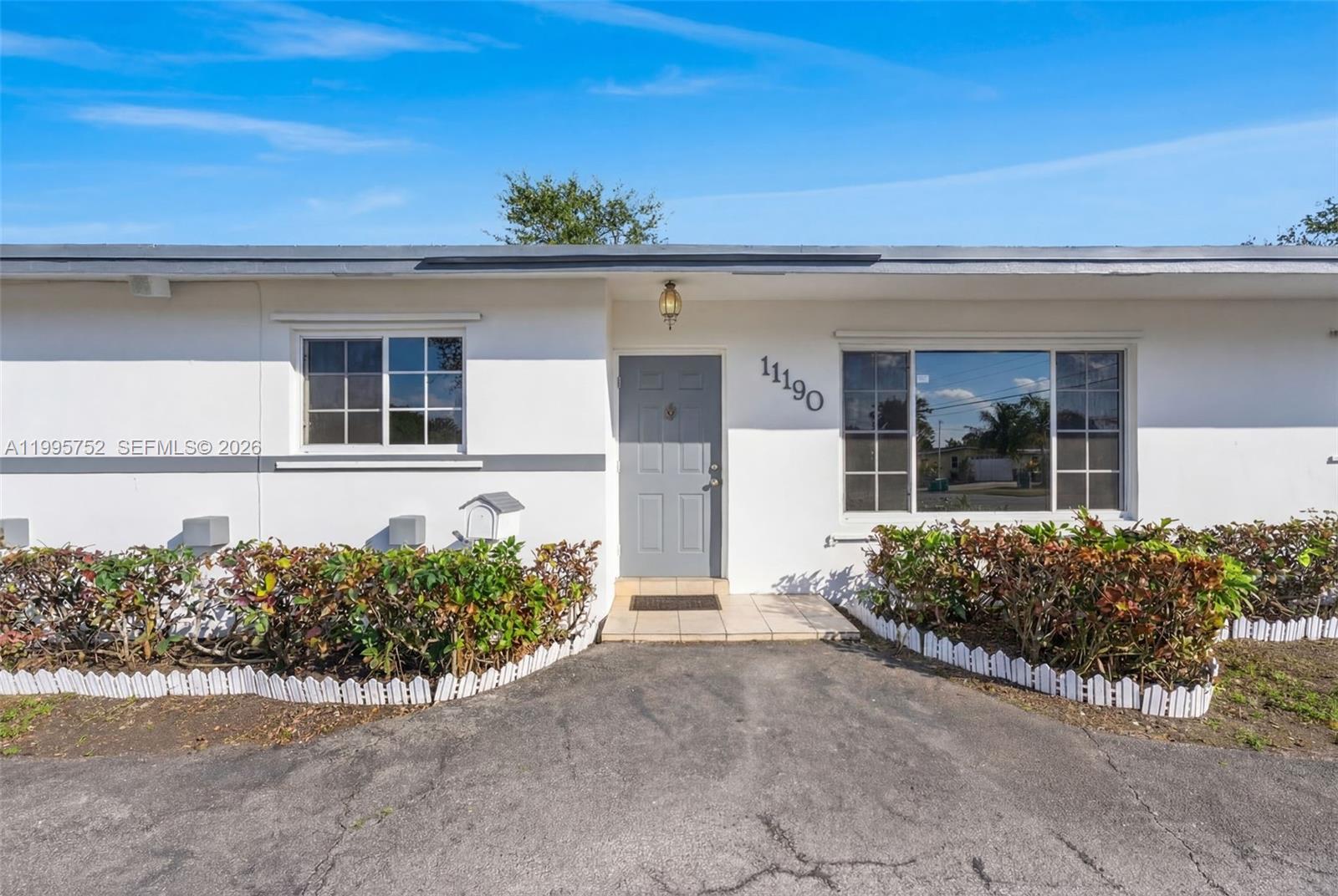 A white single-story house exterior features a gray front door and two large windows — 11190 SW 57th St, Miami FL 33173, MIAMI, FL
