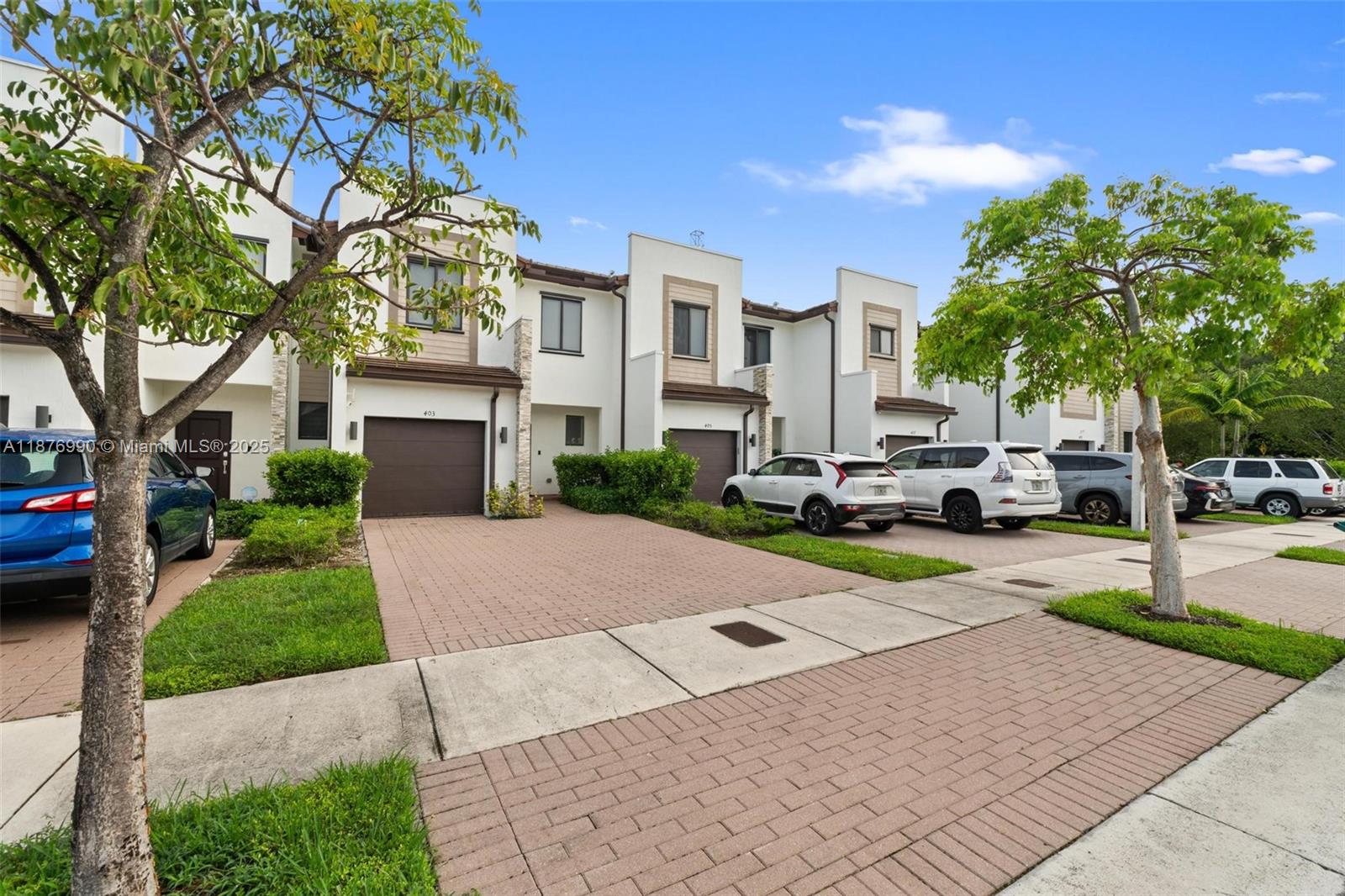 A row of modern townhouses features attached garages, brick driveways, and parked cars — 403 NE 212th St, Miami FL 33179, MIAMI, FL