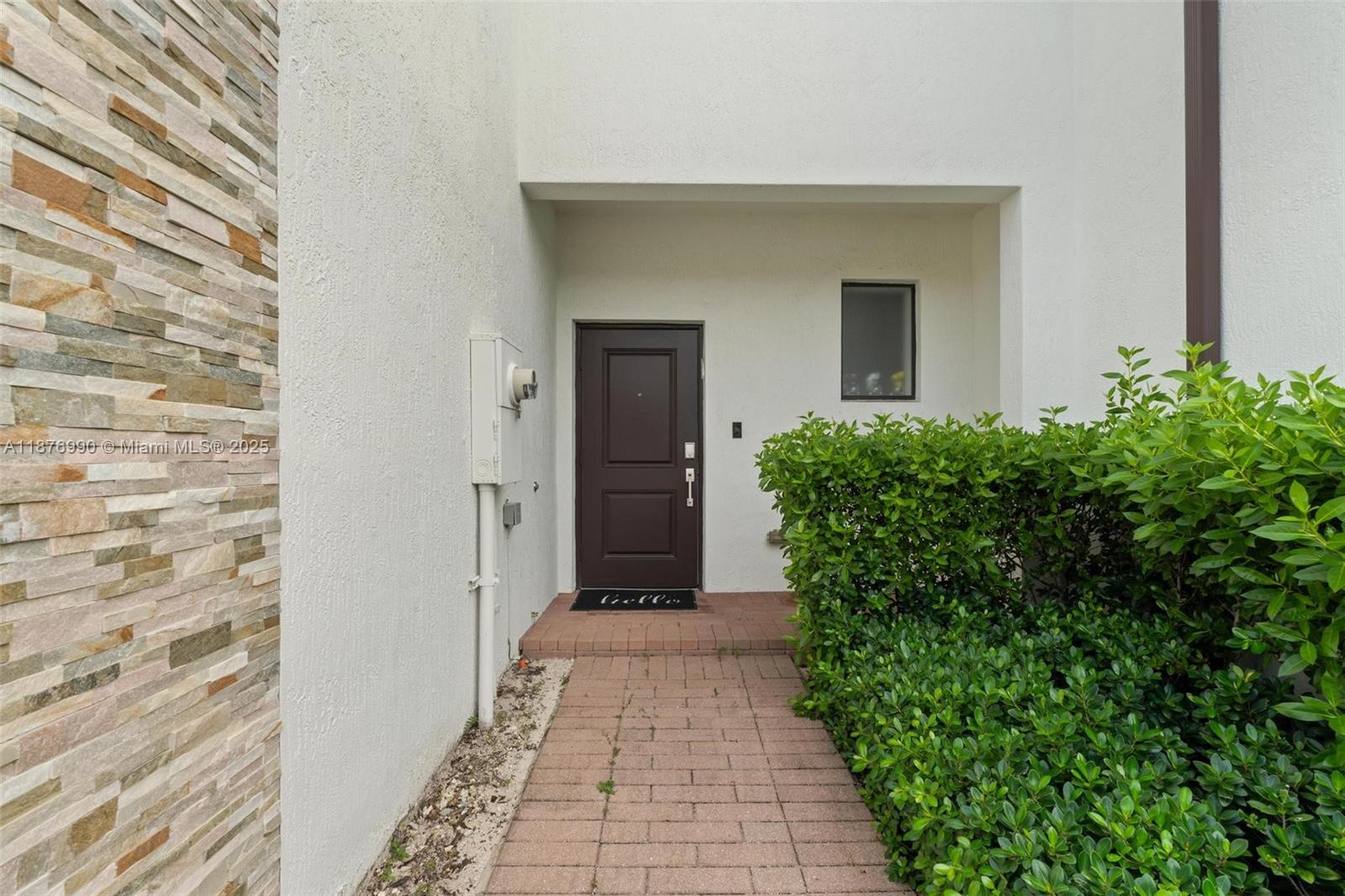 A brick walkway leads to a dark brown front door beside a stone-accented wall — 403 NE 212th St, Miami FL 33179, MIAMI, FL