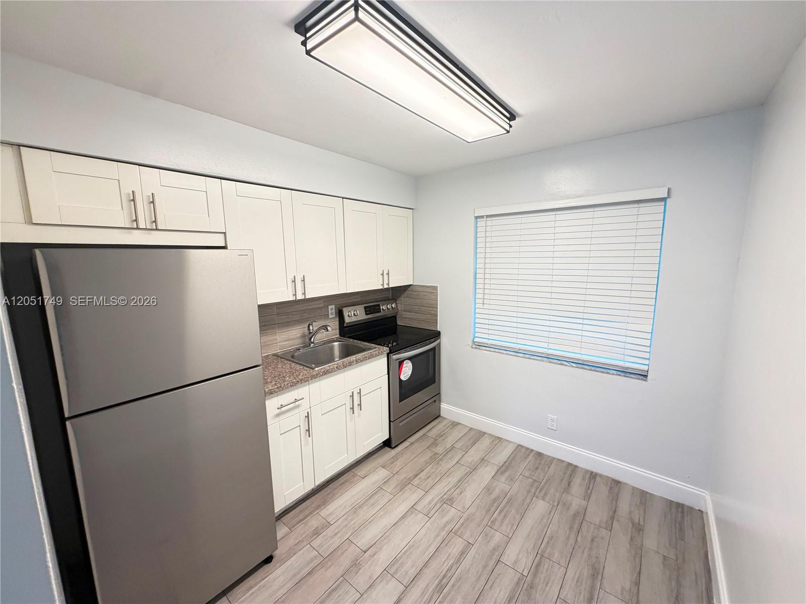 A kitchen features white cabinets, stainless steel appliances, granite countertops, and wood-look tile flooring — HOLLYWOOD, FL