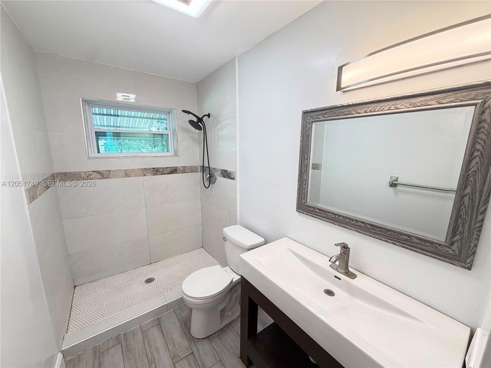 A bathroom features a walk-in shower, a toilet, and a vanity with a mirror — HOLLYWOOD, FL