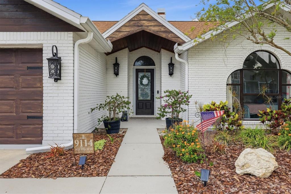 The exterior of a white brick house features a dark wood garage door and entryway — 9114 16TH AVENUE CIRCLE NW, BRADENTON, FL