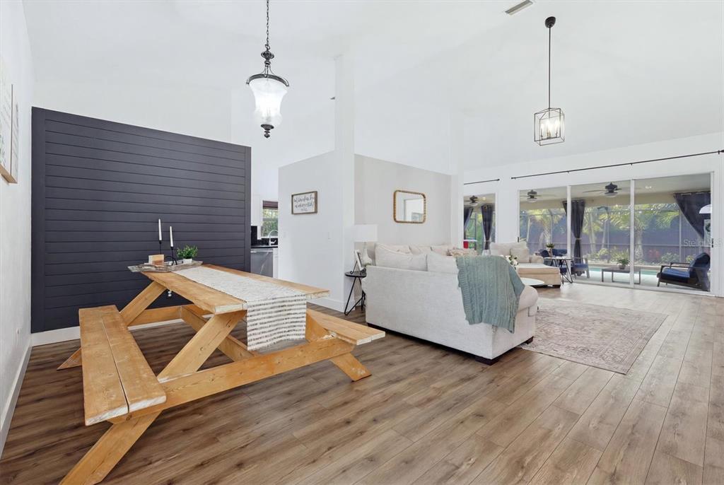 A dining area with a wooden picnic table sits before a living room with sliding doors — 9114 16TH AVENUE CIRCLE NW, BRADENTON, FL