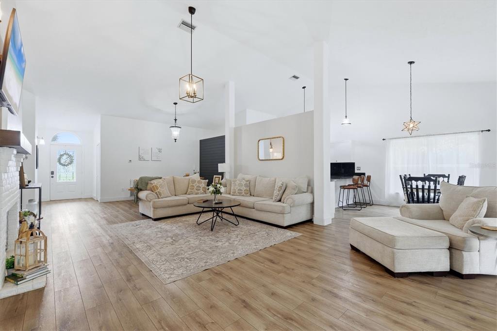 A spacious living room features light wood flooring, a large sectional sofa, and vaulted ceilings — 9114 16TH AVENUE CIRCLE NW, BRADENTON, FL