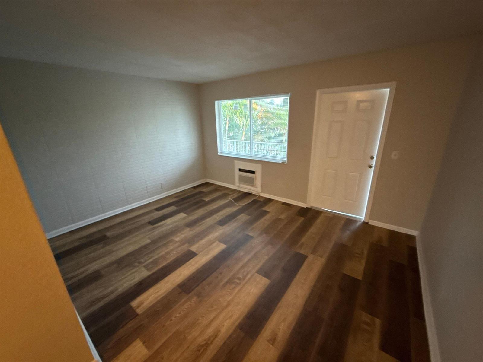An empty room features wood-look flooring, a window with an air conditioning unit, and a door — 717 NE 10th Avenue # 06, Boynton Beach FL 33435, BOYNTON BEACH, FL